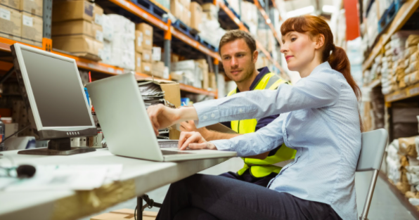 Manufacturing professional pointing at a laptop and explaining something while a factory worker watches and listens.