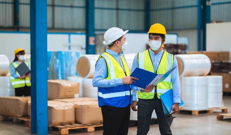 A manufacturing consultant talks to a factory worker on the work floor. 