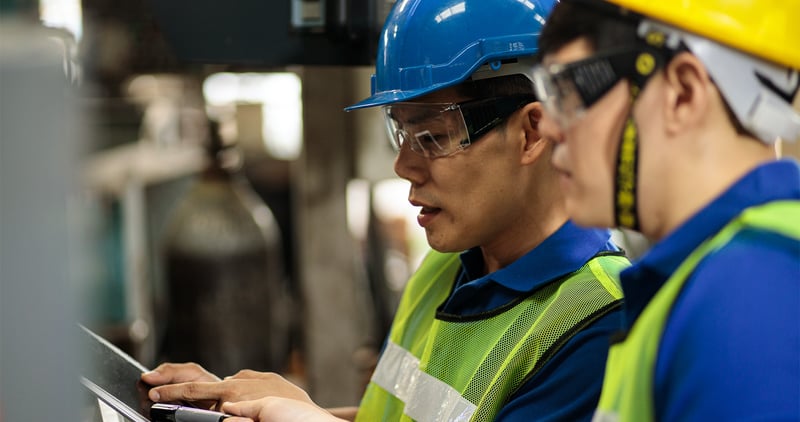 Two factory workers in uniform having a discussion.