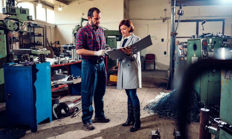 Woman writing on clipboard, man looking at clipboard in factory